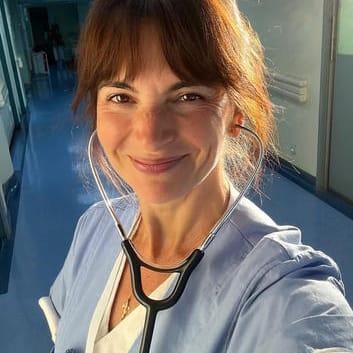 Smiling female healthcare professional in scrubs with stethoscope in hospital corridor