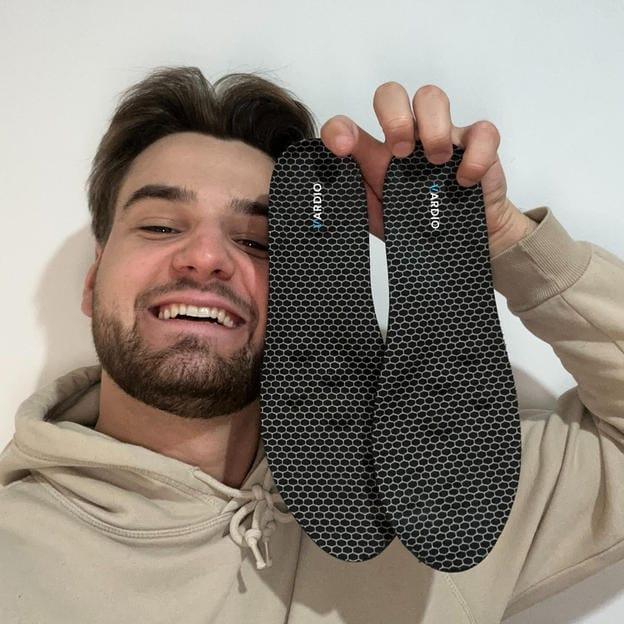 Smiling man holding a pair of black honeycomb-patterned insoles for foot comfort