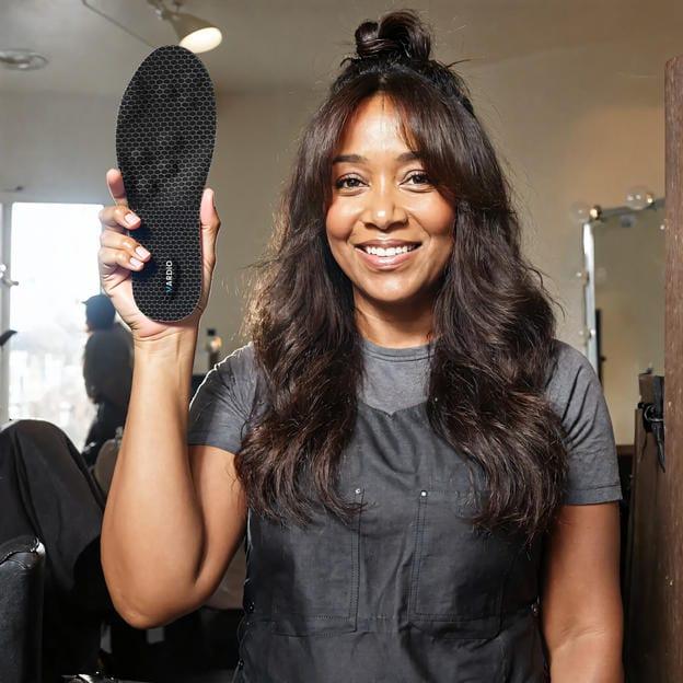 Smiling woman holding black insole, showcasing comfortable foot support indoors